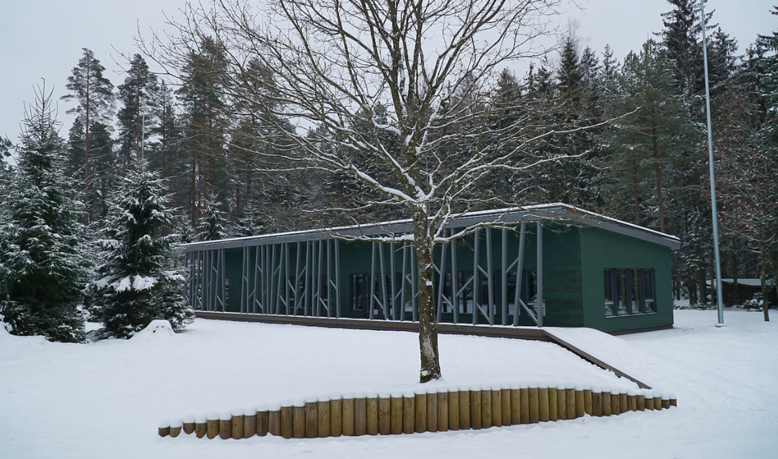 Attēlā ir ēka meža ielokā, apsniguši koki un sniegs